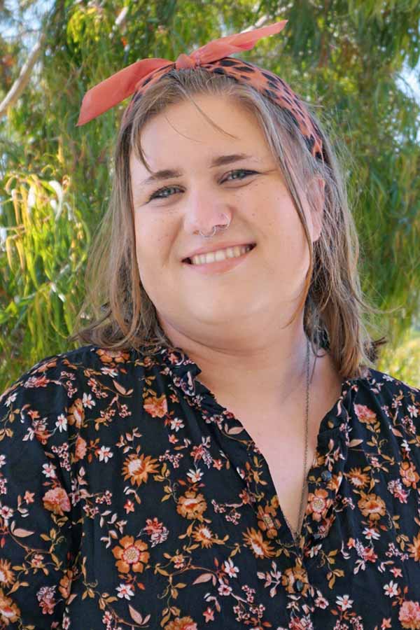 A woman with brown hair wearing a floral shirt on a green background