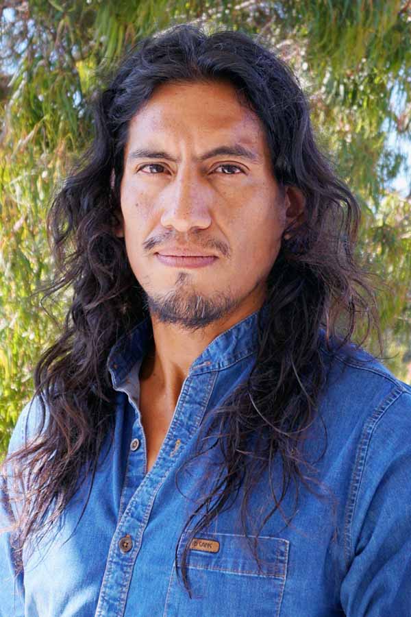 a man with long dark hair in a blue shirt on a green background