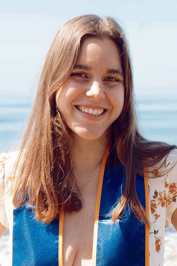 A woman with light brown hair wearing a graduation stole against a blue background