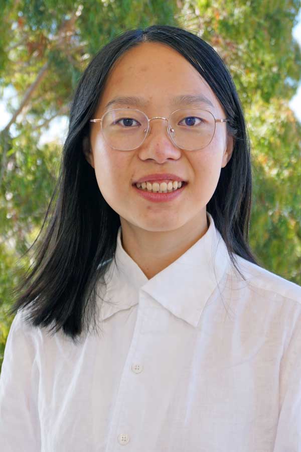 A woman with dark hair and glasses in a white shirt against a green background